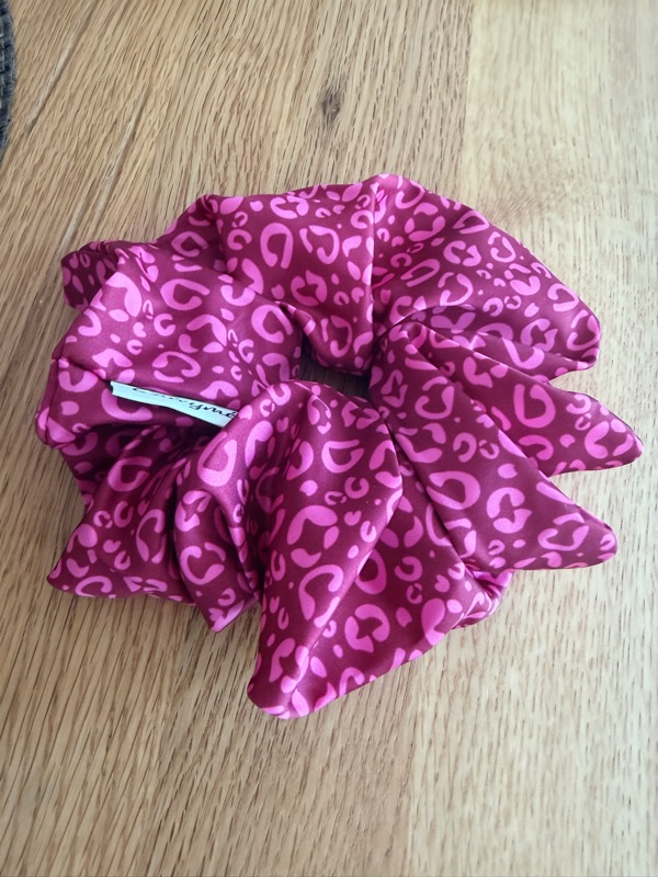 The berry red leopard scrunchie gathered on a wooden surface, the sewn-in Carimé label visible