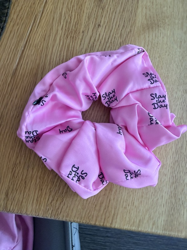 Nahaufnahme des rosa Scrunchies mit sichtbarem Schriftzugmuster