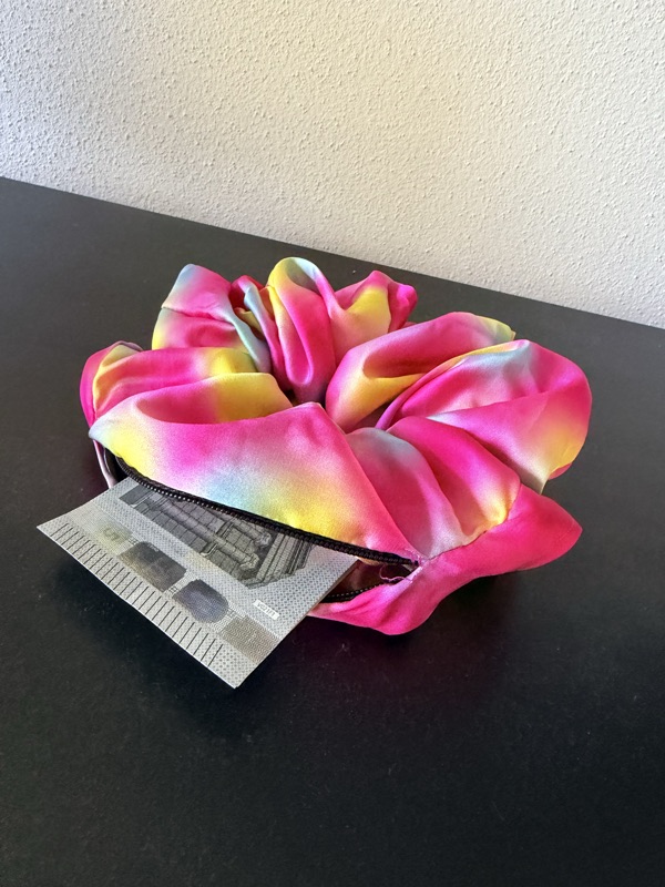 The Gradient scrunchie with its zip open and a folded banknote sticking out